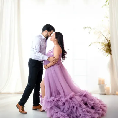 A romantic moment between expecting parents in a light and airy studio setting. The mother-to-be wears a stunning lilac ruffled gown, creating a soft and elegant maternity portrait.