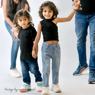 A candid and stylish shot of two young siblings holding hands in the studio, dressed in modern black tops and jeans, perfectly capturing their close bond.