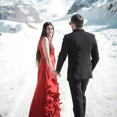 A classic romantic shot in the snows of Manali, with the bride in a striking red gown holding hands with her partner, creating a beautiful contrast against the white landscape.
