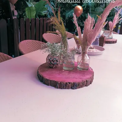 A rustic yet chic table centerpiece I created for an outdoor event. It features a slice of natural wood as the base, holding small glass vases with pampas grass and baby's breath, adding a simple and elegant touch to the guest tables.