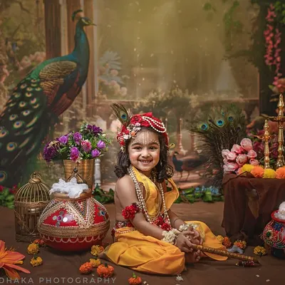 A joyful little Krishna with the most infectious smile. This shot captures the playful spirit of the theme, with a detailed set including butter pots, flowers, and a peacock backdrop.