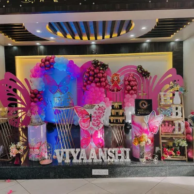 A full stage view of a vibrant butterfly-themed birthday party for 'Viyaanshi'. The setup includes large wing props, balloon columns, and personalized cutouts, creating an immersive experience.