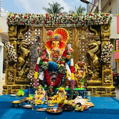The final look of our grand Ganesh pandal, ready for worship. The large Ganesha idol is framed by ornate gold pillars and a lattice screen, with thick garlands of white chrysanthemums and red roses adding to the festive look.
