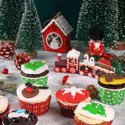 A whimsical Christmas scene with assorted cupcakes set amongst miniature trees and a toy train, creating a magical winter wonderland.