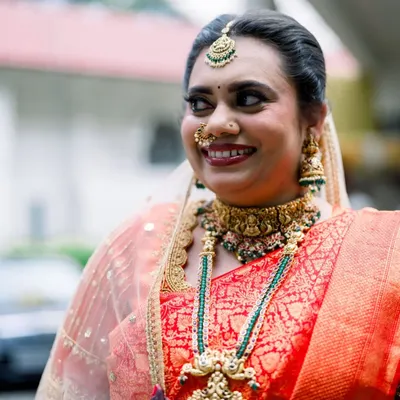 A radiant smile from our beautiful bride Suchetha. She chose a layered temple jewellery set with a statement choker and a longer haram featuring green bead accents, perfectly matching her stunning red bridal saree.