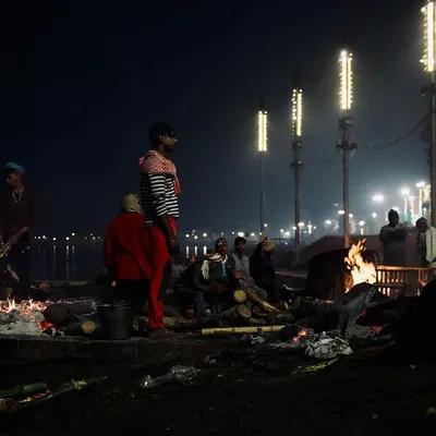 The funeral pyres of Manikarnika Ghat illuminate the night, with figures silhouetted against the flames and the distant, lit-up ghats. This image captures the somber, yet powerful, nocturnal atmosphere of the cremation grounds.