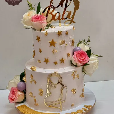 A beautiful two-tier baby shower cake with a "Oh Baby" theme. This cake is decorated with fresh flowers, gold stars, and an elegant silhouette of a mother-to-be.