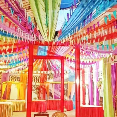 The interior of a colorful pandal designed for a festival celebration. The ceiling is covered with multi-colored fabric streamers and pennant banners, creating a joyful and energetic environment.