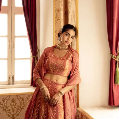 A soft, romantic portrait captured using natural window light. This image from a brand campaign highlights the delicate embroidery of the lehenga in a serene, elegant setting.