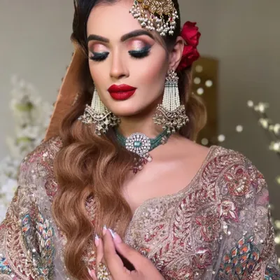 A glamorous Nikkah look featuring bold red lips and dramatic eyes. The side-swept Hollywood waves and a statement passa complete this advanced bridal makeup style.