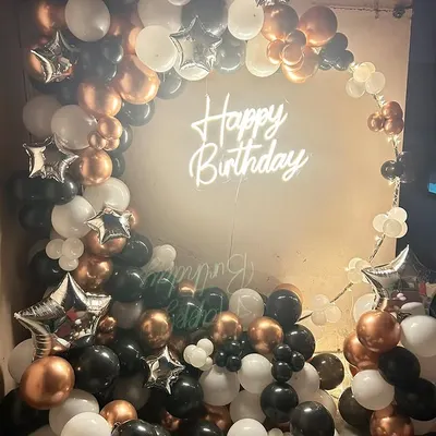 A full and luxurious balloon arch in black, white, and rose gold, with a neon sign creating a glamorous photo corner.