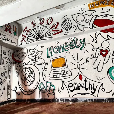 A section of the doodle mural for a CA students' hostel, featuring words like "Wisdom," "Honesty," and "Empathy." The design combines motivational text with playful icons like a rocket and a laptop to create a visually engaging and inspiring environment.