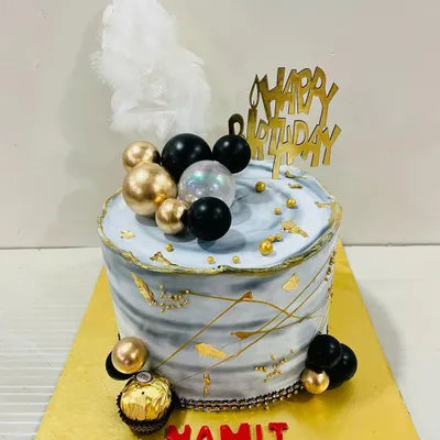 A cool and contemporary cake with a grey marble effect, accented with black and gold spheres, gold leaf, and a white feather. Perfect for a stylish celebration.