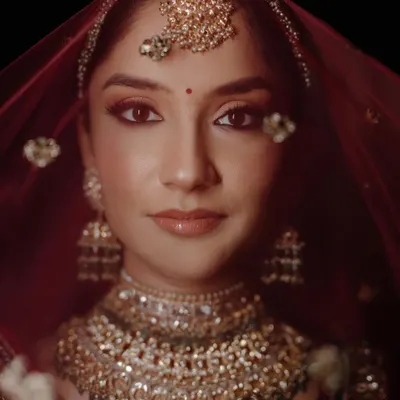 A classic bridal portrait. The direct gaze, rich colors of the red veil, and intricate jewelry come together to create a powerful and timeless image of the bride, Diksha.