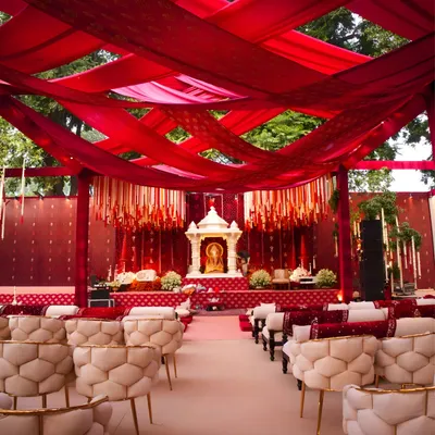 The main stage for a traditional puja, draped in rich red fabrics. The seating is arranged to provide every guest with a clear view of the ceremony, blending modern comfort with a reverent and traditional aesthetic.