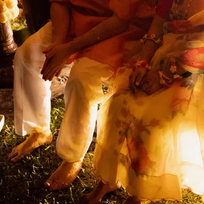 A candid detail shot from a Haldi ceremony. The couple's feet, covered in turmeric, and their intertwined hands tell a story of togetherness and tradition.