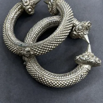 A pair of our exclusive silver leg kadas. These heavy, antique-finish pieces feature a textured body and intricately carved ends, perfect for a traditional or tribal look.