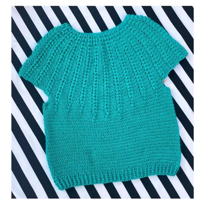 Here is the Goldenrod Sweater, a beautiful short-sleeved top made with soft cotton yarn. The textured stitch work gives it a lovely feel, and it's perfect for a casual day out. This piece is laid flat to show the full body construction before it's worn.