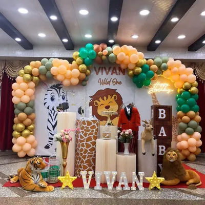 A full stage setup for a "Wild One" jungle-themed birthday. This features a custom backdrop, a balloon arch in safari tones, and a variety of plush jungle animals and themed plinths to create a complete look.