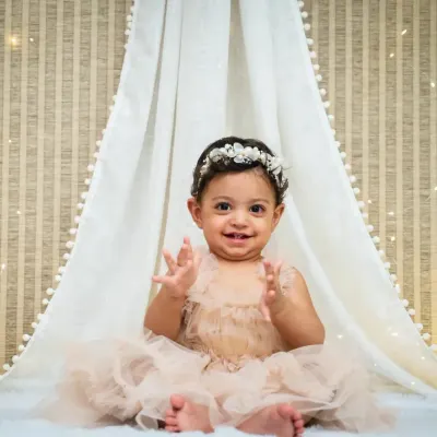 A beautiful close-up of a one-year-old girl in a peach tutu, clapping her hands with joy in a bohemian-style teepee setup.