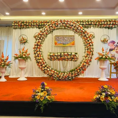 A full stage setup for a grand naming ceremony. The large floral ring creates a magnificent focal point, with coordinated flower arrangements and space for family photos.
