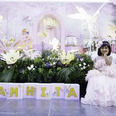 The birthday girl herself, looking like a real fairy princess in the enchanted garden I created. Seeing her smile in front of the personalized 'SAMHITA' name blocks and the detailed backdrop makes all the hard work worthwhile.