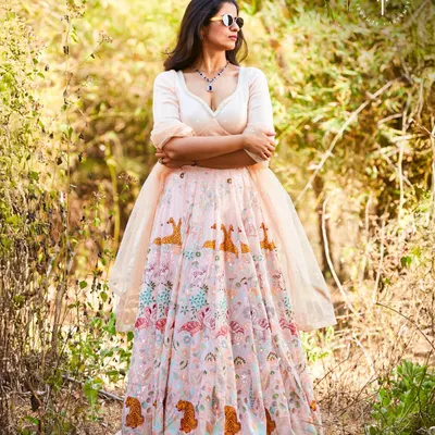 A whimsical and modern take on the lehenga. This light pink skirt features unique animal and floral motifs, paired with a simple cream blouse. It's a fresh, stylish choice for a daytime wedding or outdoor function.