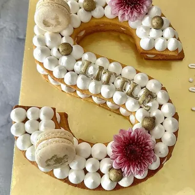 A personalized monogram tart cake for a Rakhi celebration. This 'S' shaped tart is made with a crunchy biscuit base and topped with cream, macarons, and fresh flowers.