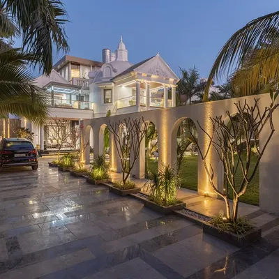 The 'Tropical Manor' at night, where landscape lighting transforms the space. The illuminated arches create a dramatic rhythm along the driveway, highlighting the carefully selected trees and framing views of the grand villa beyond.