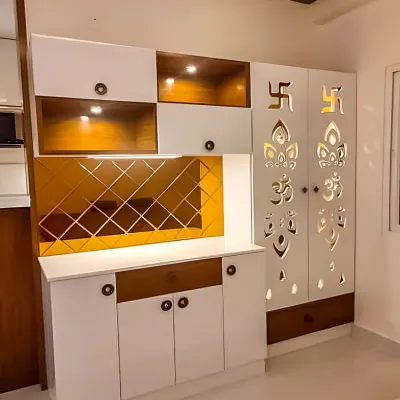 A modern pooja unit in white and wood, featuring intricate CNC-cut doors with sacred symbols like Om and Swastika. The unit includes backlit niches and a mirrored backsplash for an elegant and divine touch.