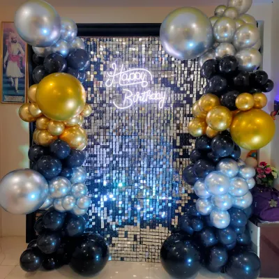 A close-up of our popular shimmer wall backdrop. This one in silver is framed by black, gold, and silver balloons and features a 'Happy Birthday' neon sign, creating a high-energy photo spot.