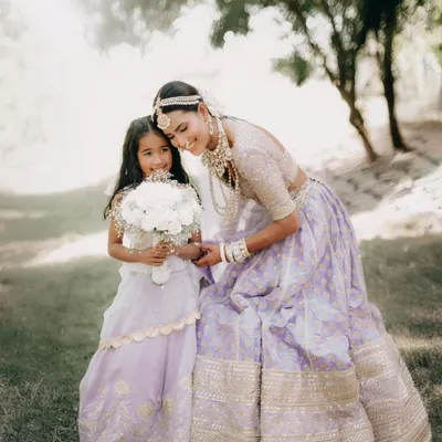 A bride in a beautiful lavender lehenga shares a sweet moment with a young flower girl. This image captures the magical connection between generations at a wedding.