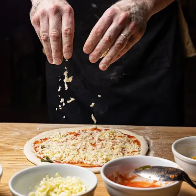 The moment it all comes together. Here, a participant in our pizza making class is adding a generous sprinkle of cheese before it heads into the oven. We provide all the fresh ingredients you need.