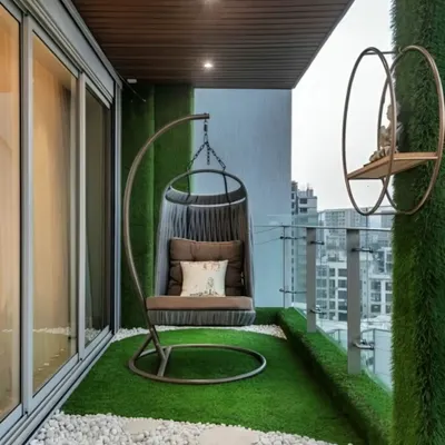 A perfect balcony retreat featuring a comfortable swing chair on an artificial grass floor. The vertical green wall adds privacy and a touch of nature in the middle of the city.
