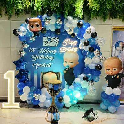 A "Boss Baby" themed first birthday party, featuring a custom backdrop with character cutouts, a blue, white, and silver balloon ring, and a light-up number '1'.