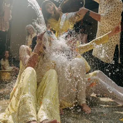 The moment the Haldi ceremony turns into a water fight. This shot of pure, uninhibited fun captures the joyous chaos and laughter that make for the best memories.