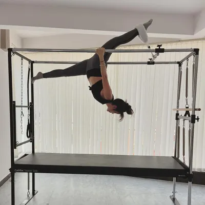 A beautiful split performed while suspended from the Cadillac bars, showcasing both strength and hamstring flexibility.
