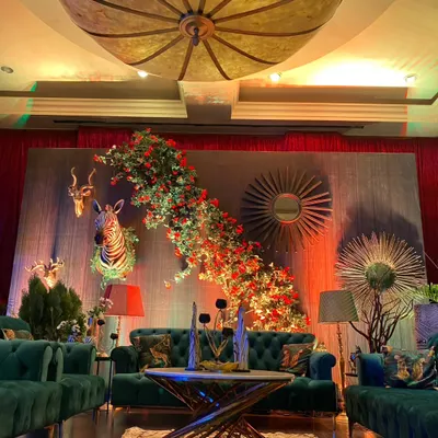 An enchanted forest Sangeet theme, featuring a lounge area with deep green velvet sofas, animal-print cushions, and a backdrop of faux animal heads and cascading florals.
