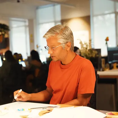 A candid shot of one of our senior architects sketching at a desk. Design is not just what you see; it is the thinking, conversations, and discoveries behind every line, a process that unfolds in our collaborative studio environment.