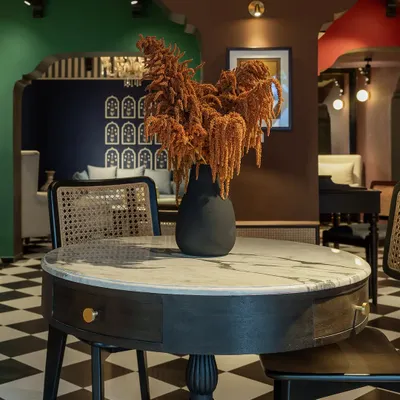 This setting from our House of Goya experience center features a marble-topped pedestal table and a caned chair against a backdrop of rich, layered colors. It demonstrates how we mix classic forms with bold, modern palettes.