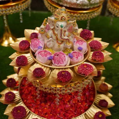A beautiful two-tiered brass stand with a Ganesha idol, surrounded by fresh lotus buds and gomphrena flowers. This is a perfect pooja centerpiece.