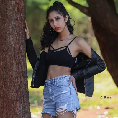 A classic street style look featuring a black crop top, leather jacket, and distressed denim shorts. The outdoor park setting with natural light gives it a relaxed, cool vibe.