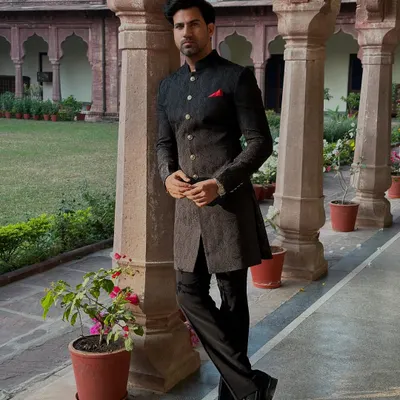 The quintessential black Achkan, presented in a regal setting. Its sharp tailoring, classic button placket, and mandarin collar create an aura of dignified elegance, perfect for any formal event.