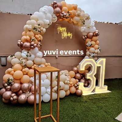 This is a chic outdoor setup for a 31st birthday, featuring a circular balloon arch in nude, white, and rose gold tones. The design is completed with a "Happy Birthday" neon sign and large light-up marquee numbers.