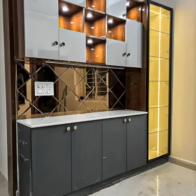A sophisticated crockery unit featuring a mix of materials. The design includes backlit wooden display niches, sleek gray cabinets, a mirrored backsplash, and a tall, yellow-tinted glass cabinet for a pop of color.
