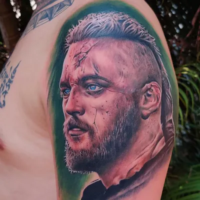 A hyper-realistic color portrait tattoo of a character from the show 'Vikings', done by guest artist Guru Pujar at our studio. The detail in the eyes and skin texture showcases a high level of skill.