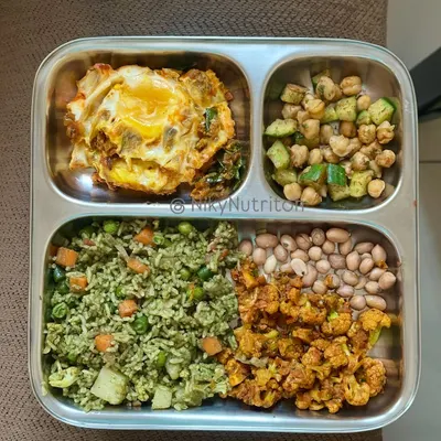 A true high-protein powerhouse plate. This meal features vegetable rice, a masala fried egg, roasted cauliflower, boiled peanuts, and a chickpea salad.