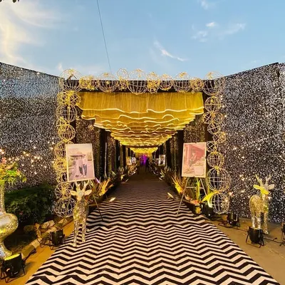 A truly modern and glamorous entrance. I used walls of silver sequins, a ceiling of wavy golden fabric with integrated lighting, and a bold black-and-white chevron carpet to create a high-impact walkway for guests.