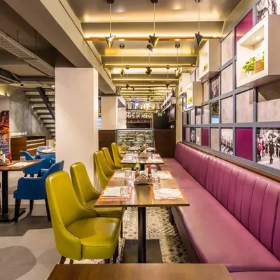 A long shot of the main dining hall at Pasta Street, Cunningham Road, showing the linear arrangement of seating. The combination of plush pink booth seating and colorful chairs creates a dynamic and comfortable environment for diners.