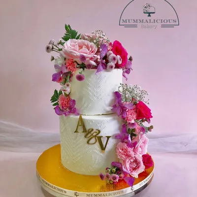 A cascade of fresh, vibrant flowers makes this two-tiered wedding cake a breathtaking centerpiece. The textured frosting and custom initial topper add a personal and modern touch to this romantic design.